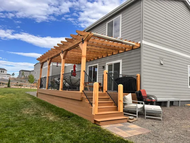Cedar pergola deck with stairs and black metal railing beside the house