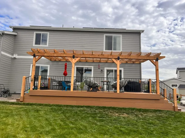 Full-width backyard deck with a cedar pergola and black metal railing