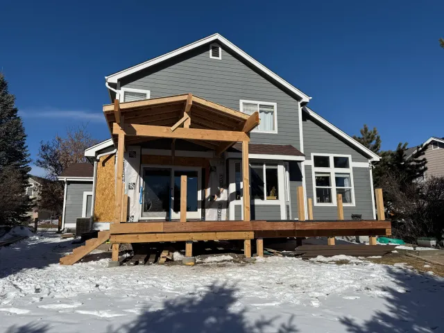 Gabled timber porch-cover frame over a deck under construction, snow on the ground
