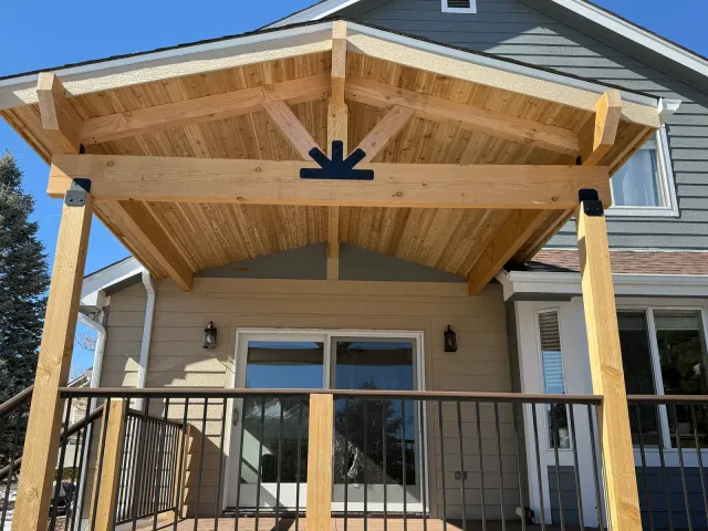 Gabled timber patio cover with exposed beams over a deck with black railing