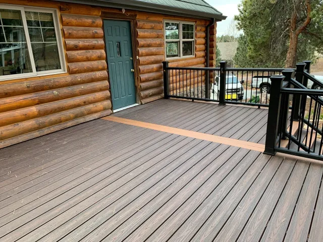 Brown composite deck with black metal railing beside a log home