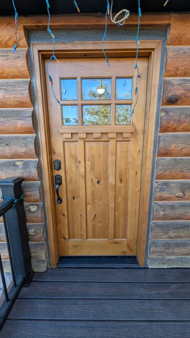 Wood front door with a divided-light window set into a log wall