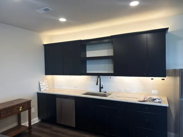 Kitchenette with navy shaker cabinets, open shelving, and under-cabinet lighting