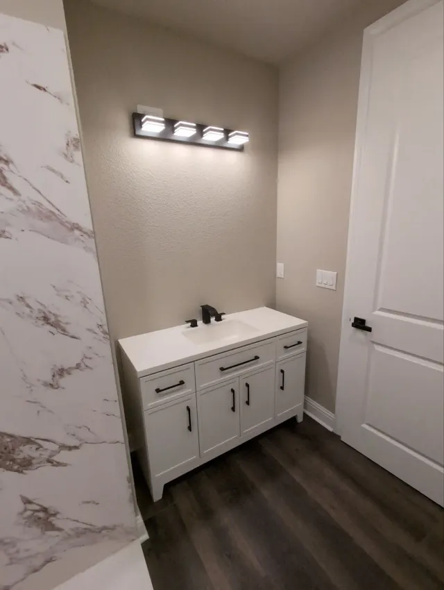 Bathroom vanity with a white cabinet beside a marble-look tile wall