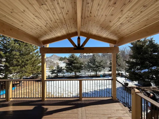 View from under a gabled timber deck cover toward a snowy backyard