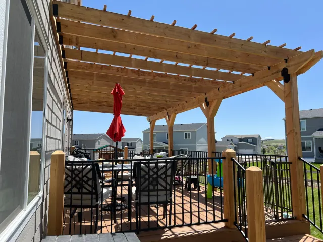 Wood pergola over a deck with black metal railing and a patio dining set