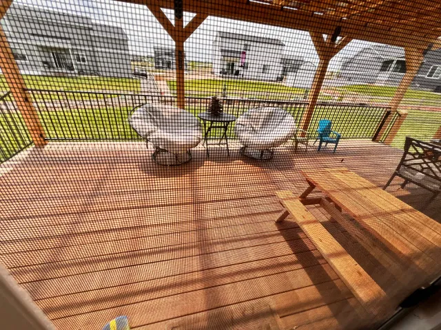 Deck under a stained wood pergola with lounge chairs and a picnic table