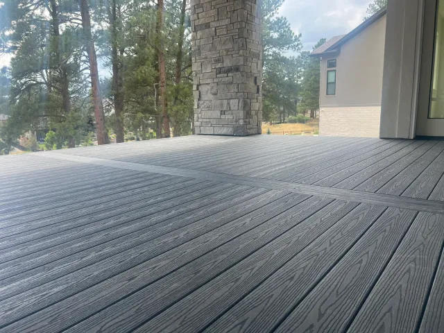 Dark gray composite deck beside a stone chimney, with pine trees beyond
