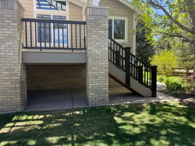 Elevated deck with black railing and stairs, supported by brick columns