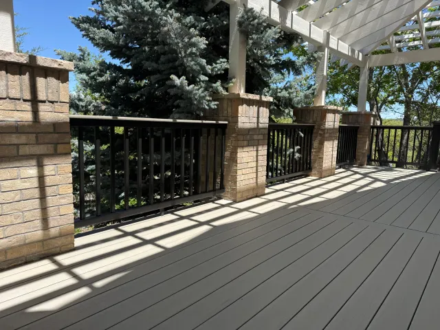 Composite deck under a white pergola with brick columns and black railing