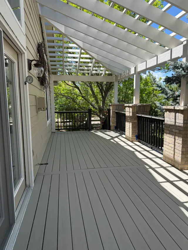 White pergola over a long composite deck running alongside the house