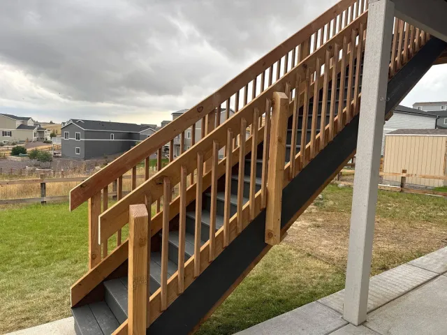 Exterior wood stair with stained railing up to a second-story deck