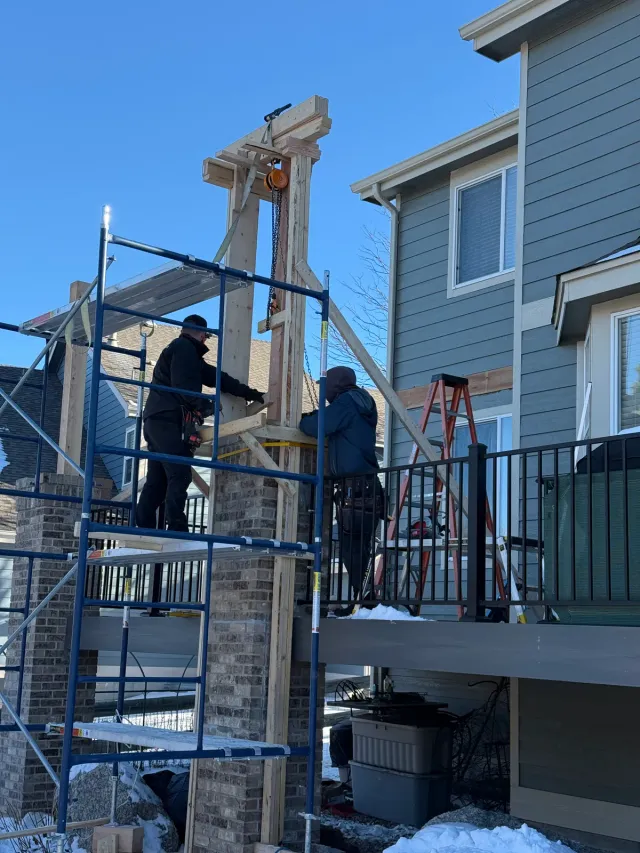Crew on scaffolding hoisting a timber post onto a brick column for a deck cover