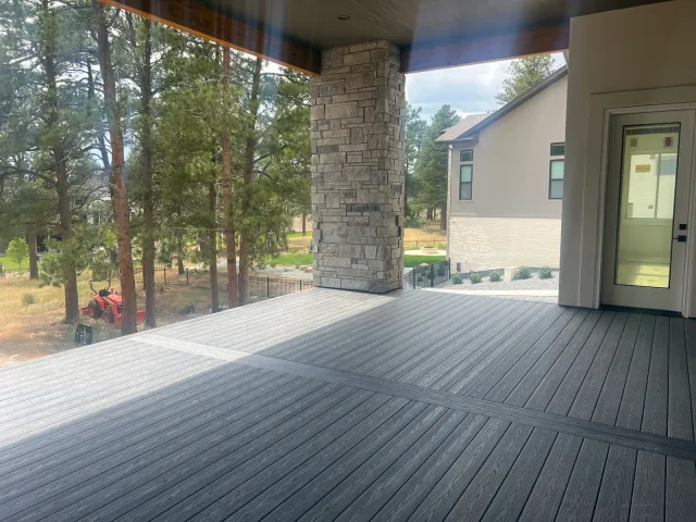 Covered composite deck with a stone-clad column, pine trees beyond