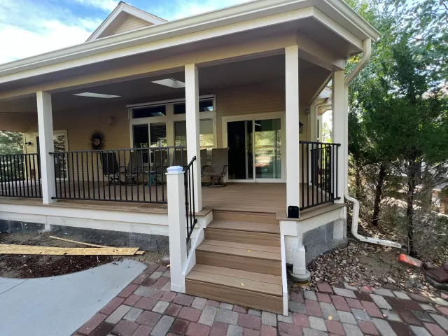 Covered porch with white columns, black railing, and wood steps