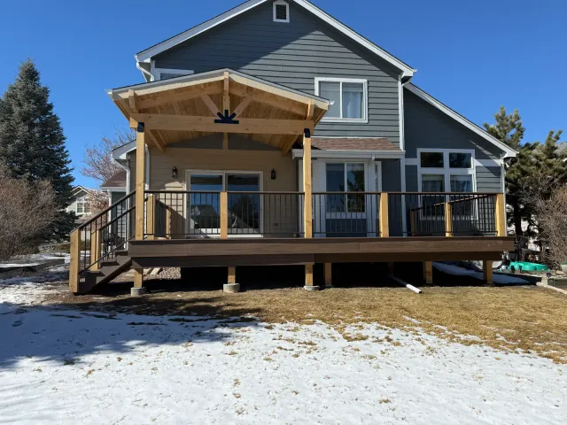 Gabled timber cover over a rear deck with black railing, snow in the yard
