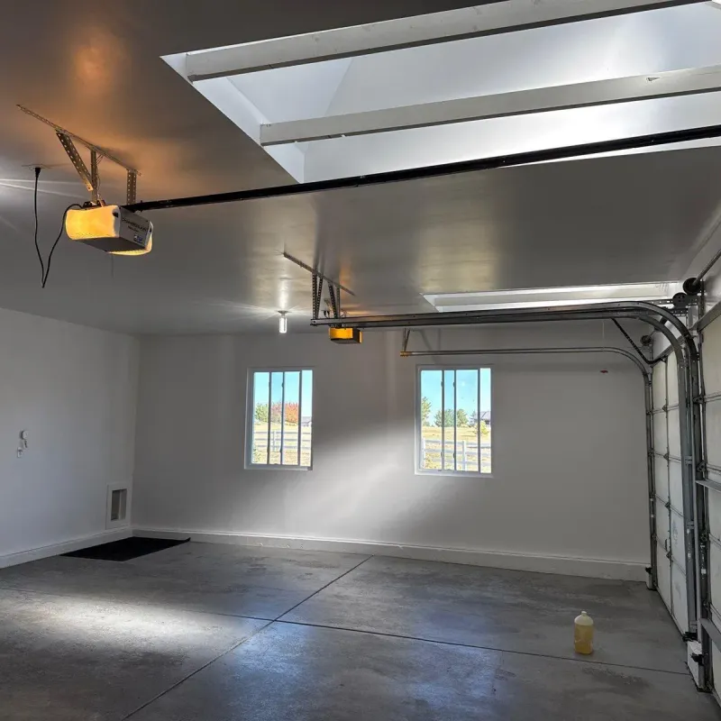 Finished garage with white painted walls, skylights, and garage door openers