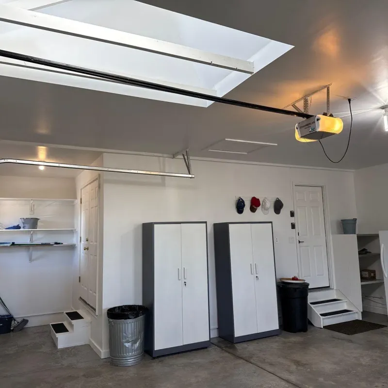 Finished garage wall with storage cabinets, shelving, and steps to the house door
