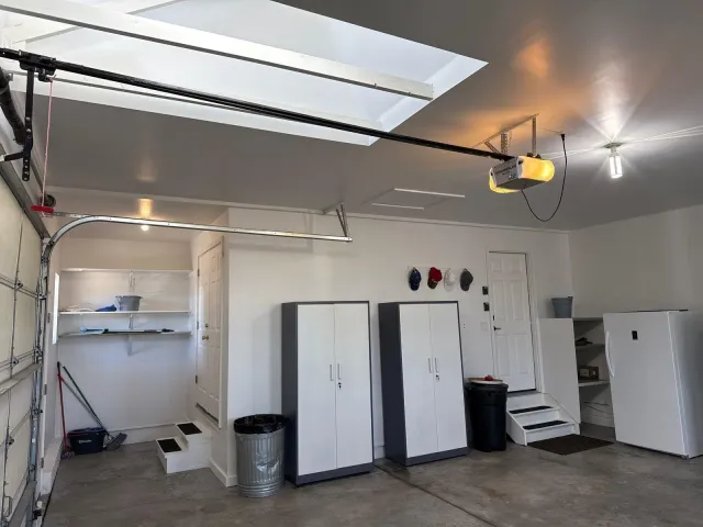 Finished garage wall with storage cabinets, shelving, and steps to the house door