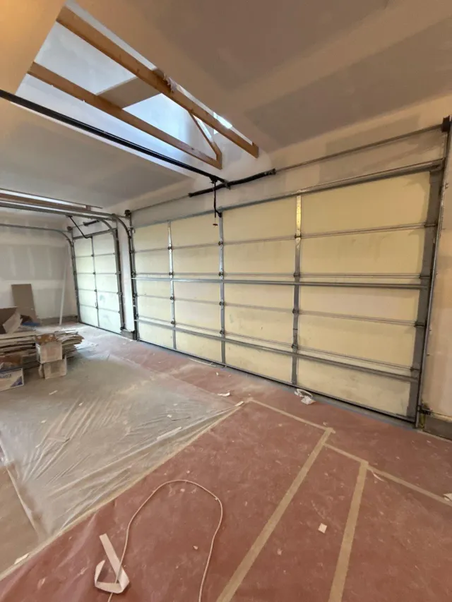 Garage during drywall work, with the floor protected by paper and plastic