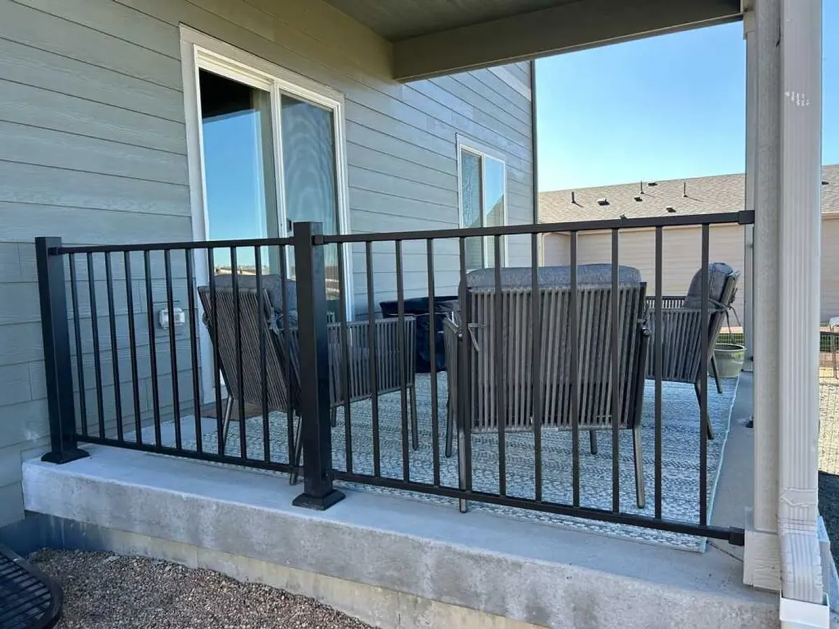 Black metal railing around a covered concrete porch with patio chairs