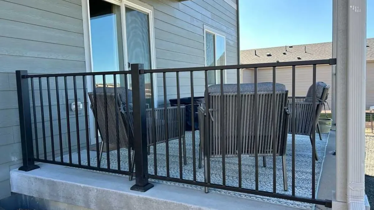 Black metal railing around a covered concrete porch with patio chairs