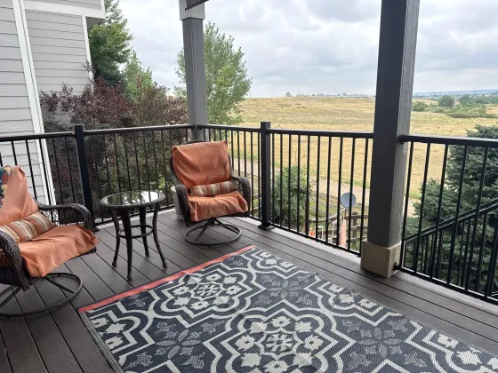 Covered deck seating area with dark composite boards and black railing, open space beyond