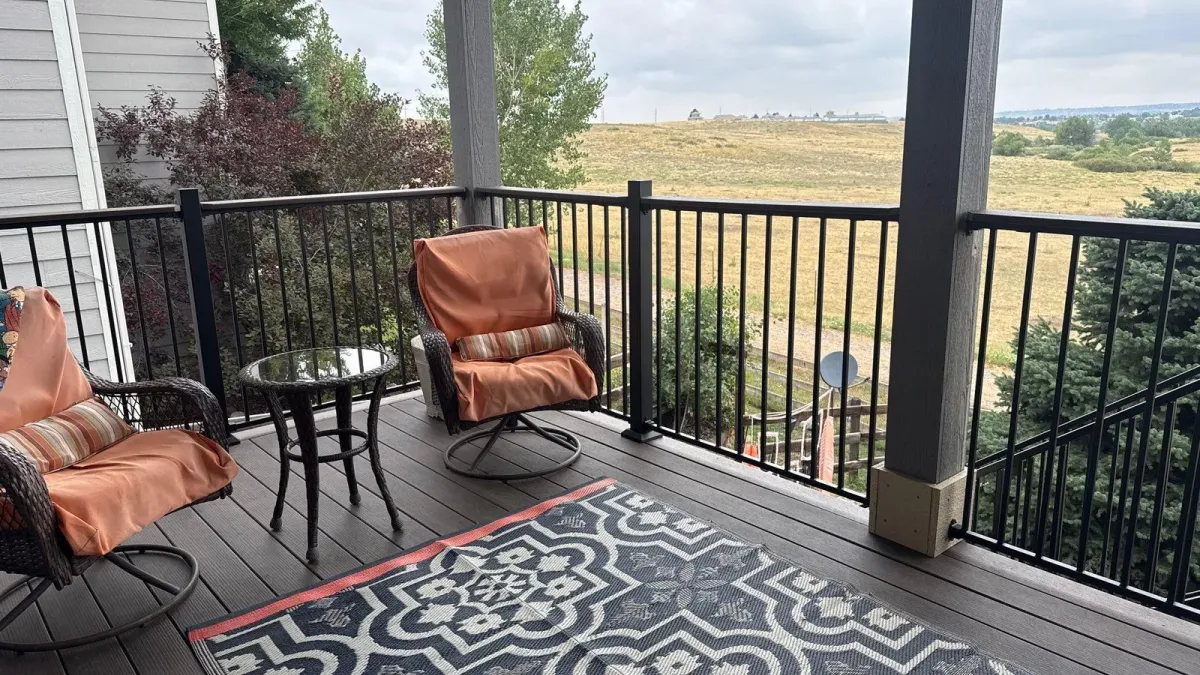 Covered deck seating area with dark composite boards and black railing, open space beyond