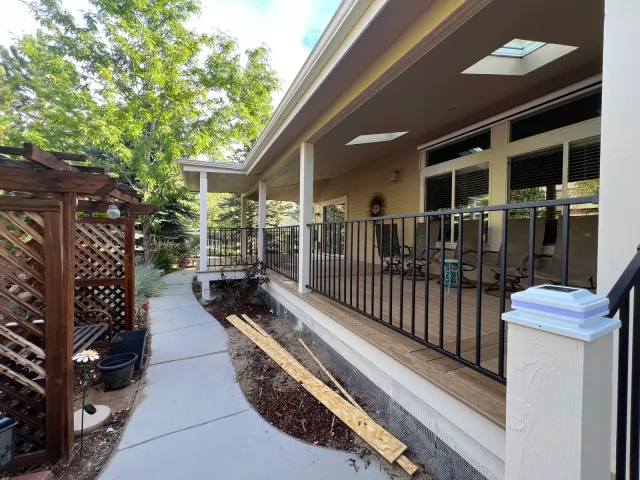 Long covered porch with black railing beside a garden walkway and lattice screen