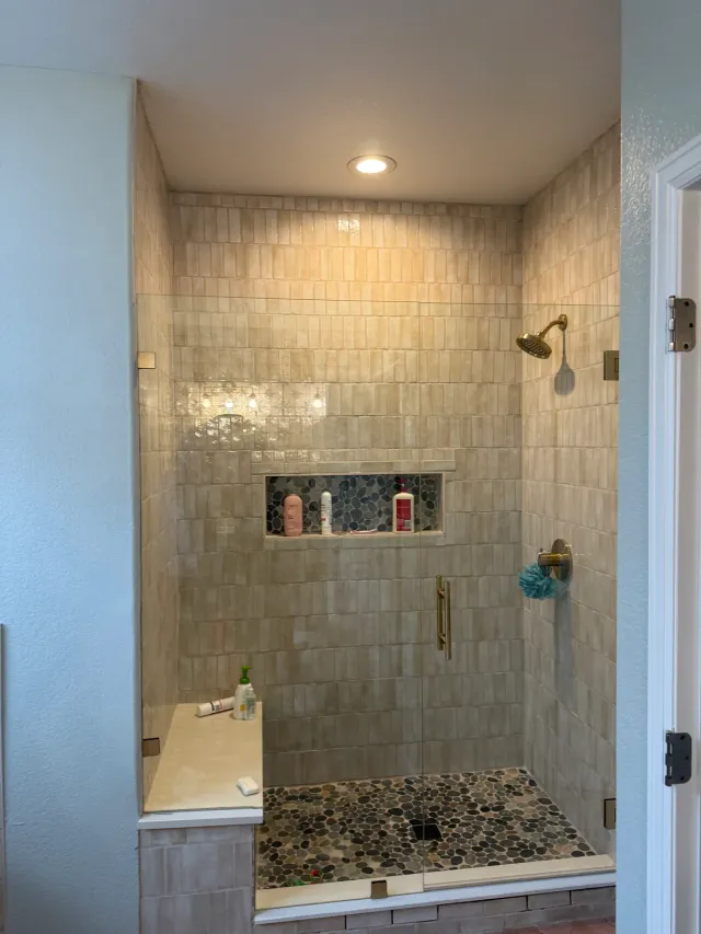 Walk-in shower with handmade-look tile, a pebble floor, and a recessed niche